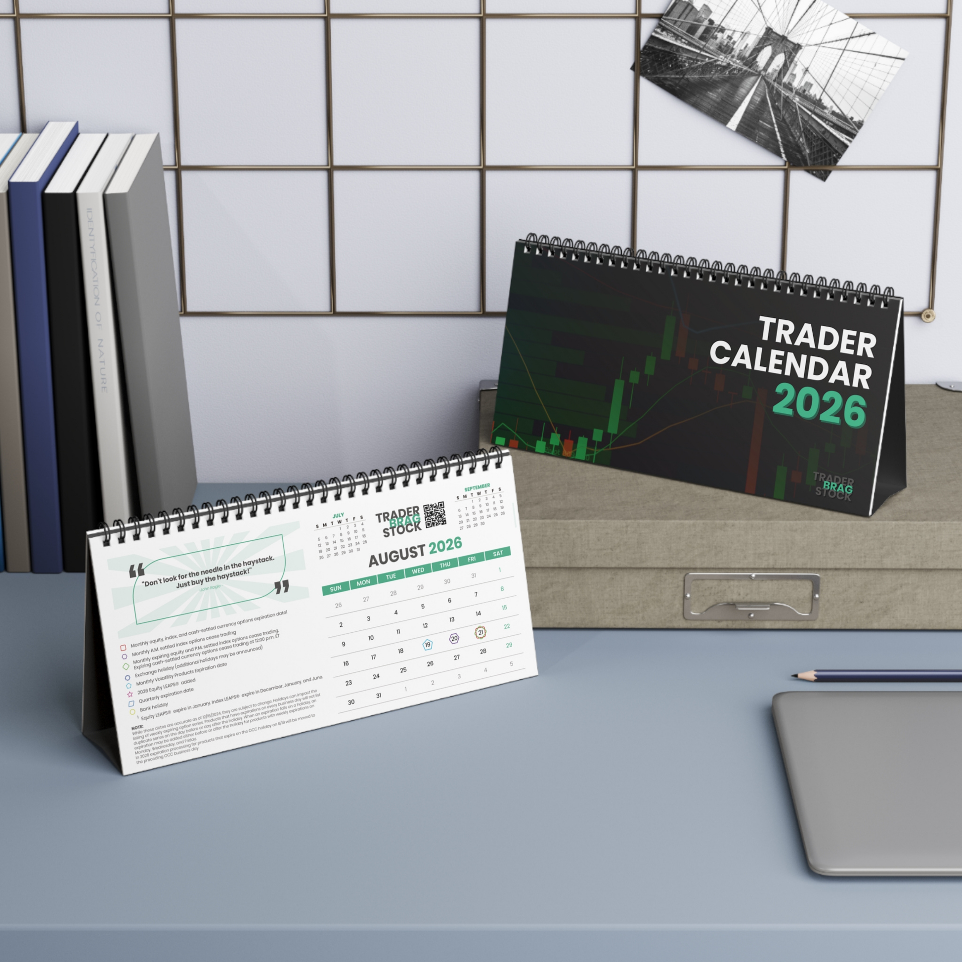 Two spiral-bound calendars titled 'Trader Calendar 2026' on a desk with books and a pen.