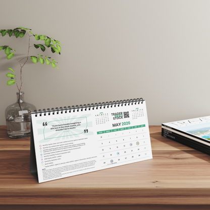 Tabletop trader calendar on a wooden surface with a plant and book in the background